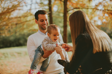 Happy young parents have fun with baby boy in autumn parkの写真素材