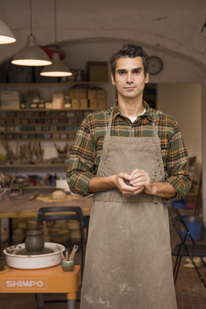 Portrait of handsome young man in pottery workshop holding clayの写真素材