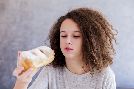 Portrait of curly hair teen girl eating croissantの写真素材