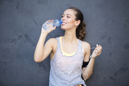 Portrait of young athletic woman drinking water by the wallの写真素材
