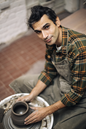 View at an artist makes clay pottery on a spin wheel in workshopの写真素材