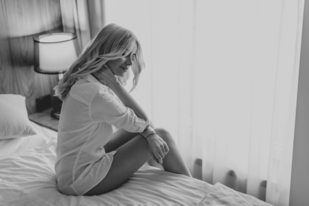 Young blonde woman sitting on the bed in the room looks melancholyの写真素材