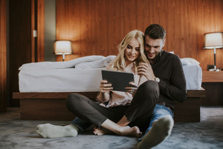 Happy loving couple sitting on the floor with digital tabletの写真素材