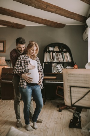 Pregnant woman and happy man in the house standing hugged in the roomの写真素材
