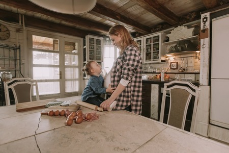 Pregnant woman and little daughter in the rustic kitchen preparing meal