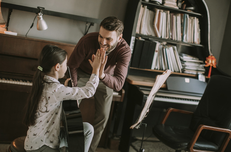 Cute little girl with guitar teacher in the room at homeの写真素材