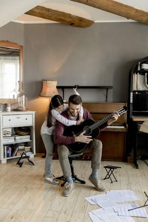 Man playing acoustic guitar for daughter in living room at homeの写真素材