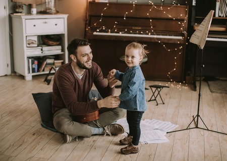 Young father and little daughter playing acoustic guitar in the room at homeの写真素材