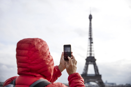 Young man with backpack taking photograph with mobile phone of Eiffel Tower in Paris, Franceの写真素材