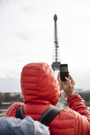 Young man with backpack taking photograph with mobile phone of Eiffel Tower in Paris, Franceの写真素材