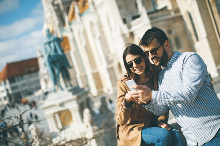 Portrait of young loving couple of tourist in town using mobile phoneの写真素材