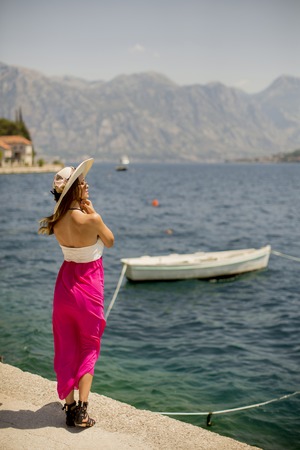 Pretty young attractive woman with a hat poses by the sea in the summer