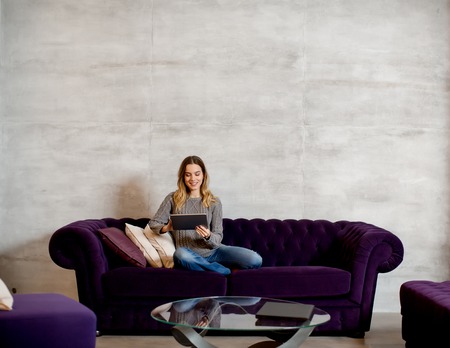 Pretty young woman with digital tablet on sofaの写真素材