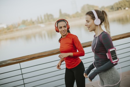 Two young women running by the river in the morningの写真素材