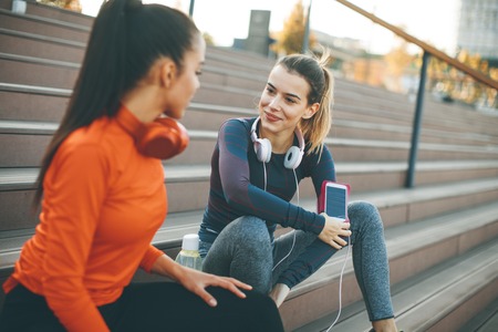 Two young attractive female runner taking break after jogging outdoors