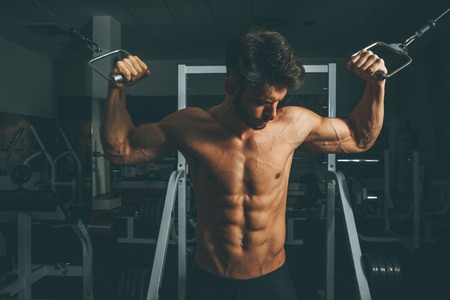 Half-naked muscular man in gym doing exercises for biceps