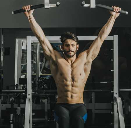 Half-naked young man doing pull ups in the gym