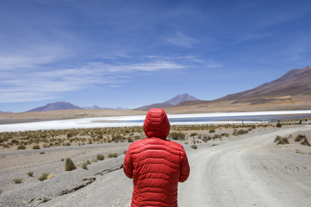 Young man lookinag at lagoon and mountains at Eduardo Avaroa Andean Fauna National Reserve in Boliviaの写真素材