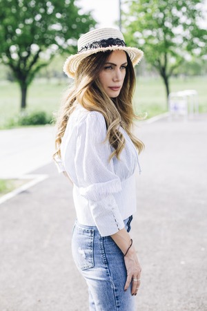 Portrait of a beautiful elegant woman with hat posing in the park at sunny summer dayの写真素材