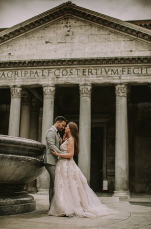 Young attractive newly married couple walking and posing in Rome with beautiful and ancient architecture on the background on their wedding dayの写真素材