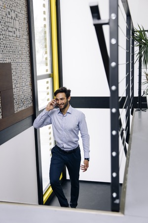 Young businessman talking on mobile phone and climbing on the stairs in modern office