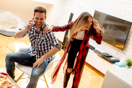 Young couple eating pizza at home and having funの写真素材