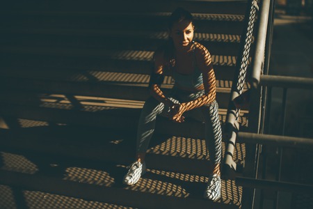 Portrait of pretty young female runner resting on the stairsの写真素材