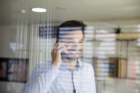Handsome young man using mobile phone behind the glass in the officeの写真素材