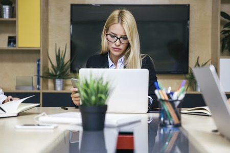Pretty young blonde woman working on laptop in the office