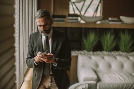 Portrait of senior handsome businessman using cell phone in modern officeの写真素材