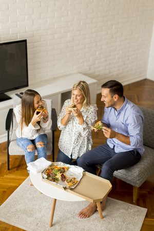 Happy friends eating pizza and having fun in the living room at homeの写真素材