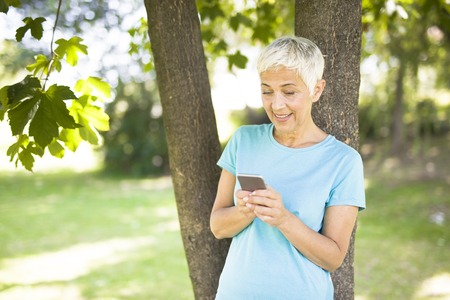 Portrait of sporty senior woman using mobile phone in the park