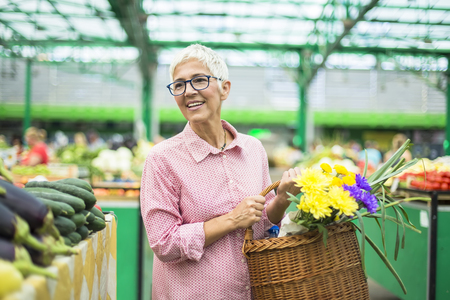Portrait of senior woman holding basket with bouquet of flowers on marketの写真素材