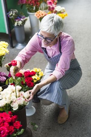Charrming senior woman arranges flowers on local marketの写真素材