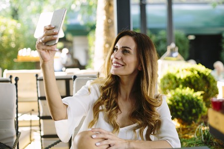 Attractive young woman with smart phone sitting in restaurantの写真素材