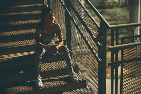 Portrait of pretty young female runner resting on the stairsの写真素材