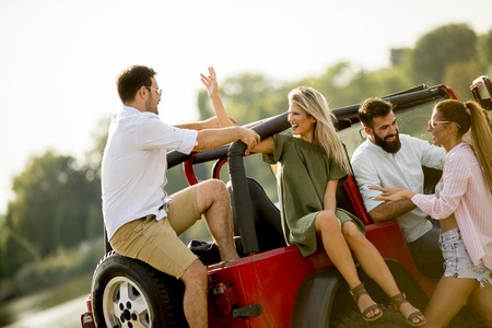Four young people having fun in convertible car by river