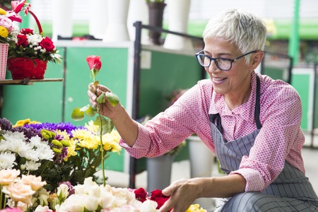 Charrming senior woman arranges flowers on local marketの写真素材