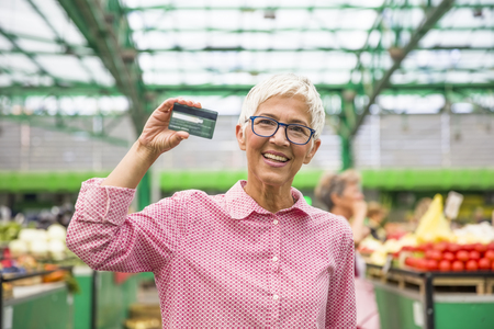 Portrait of senior woman holds credit card on marketの写真素材
