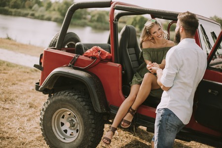 Young woman and man having fun outdoor near car at summer dayの写真素材