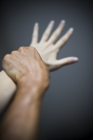 Studio shot of man holding female hand in the act of violenceの写真素材