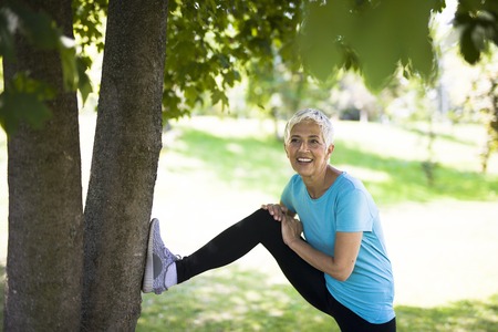 Senior woman does stretching exercise in the park by tree