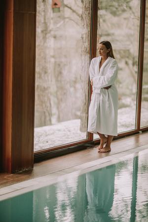 Pretty young woman in bathrobe standing by swimming poolの写真素材