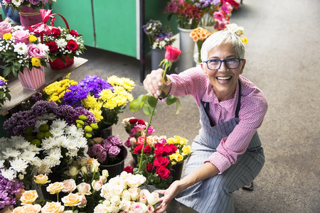 Charrming senior woman arranges flowers on local marketの写真素材