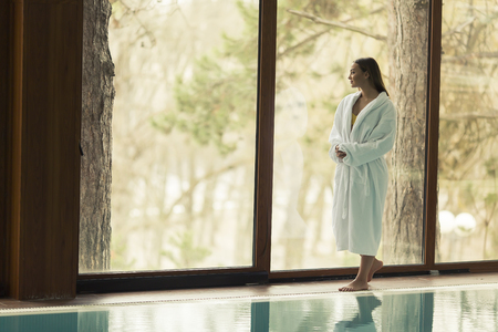 Pretty young woman in bathrobe standing by swimming poolの写真素材