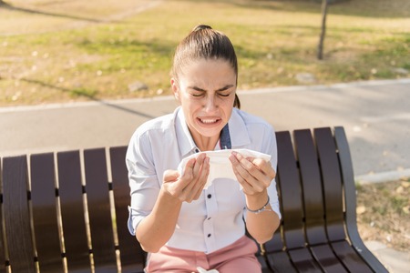 Young woman sneezing outdoor while having an allergyの写真素材