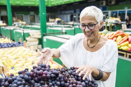 Portrait of senior woman chooses red grapes at the marketの写真素材