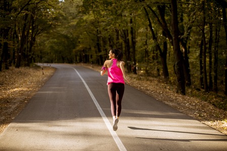Young fitness woman running at forest trail in golden autumn