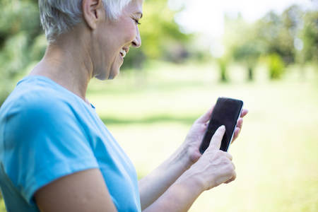 Portrait of senior woman in sports clothing  using smart phone outdoorの写真素材