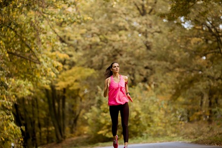 Young fitness woman running at  forest trail in autumnの写真素材